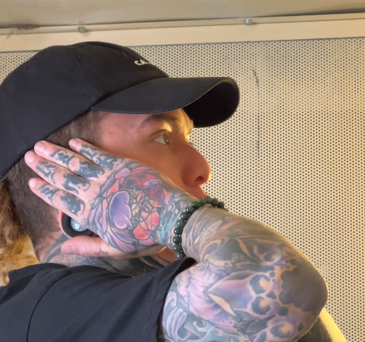 Person with full sleeve tattoos cups his ears and yells in a recording booth.