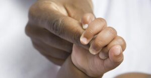 A baby hand holding an adult's finger